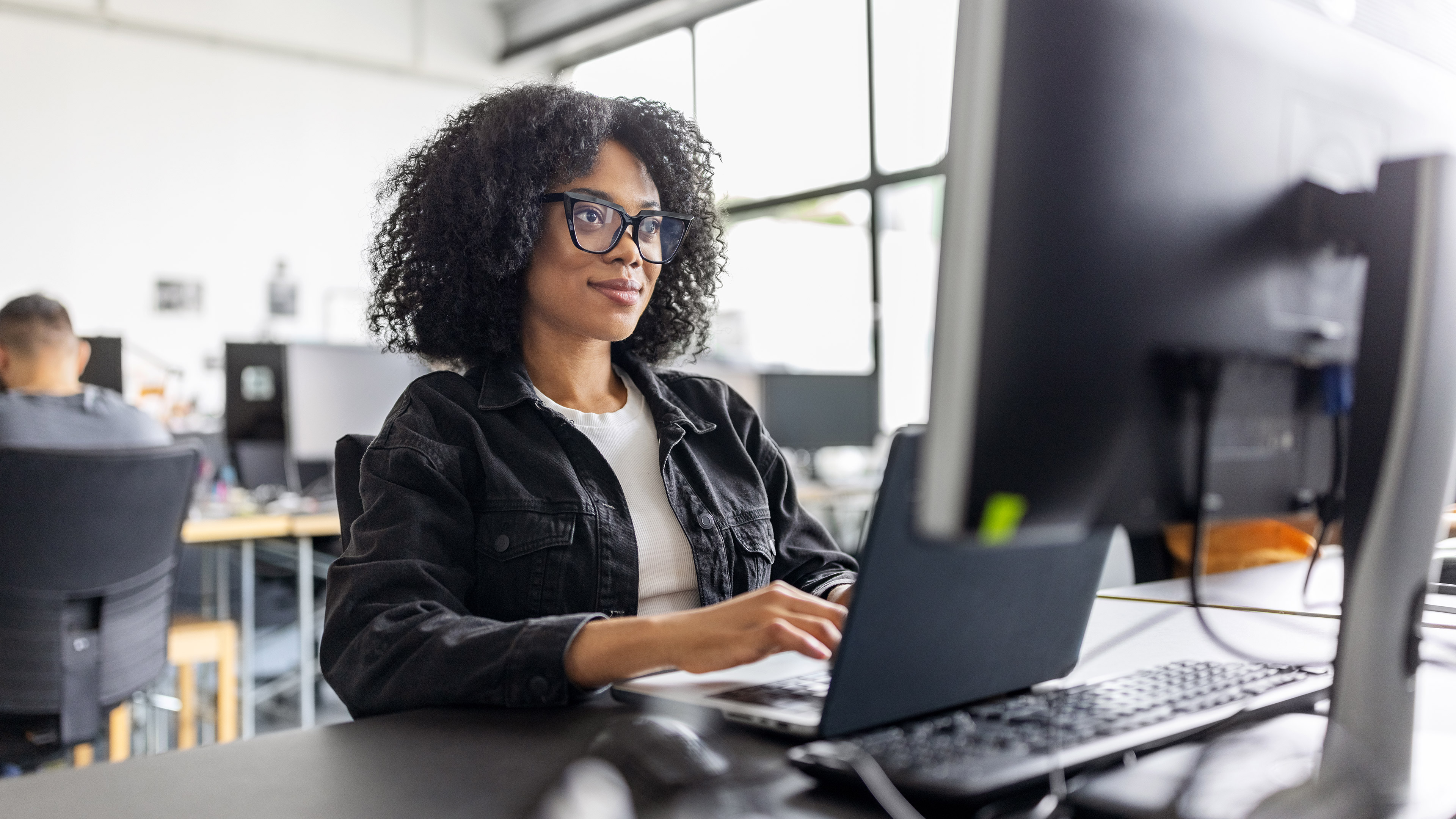 A female office worker in front of a computer, typing on a keyboard and smiling