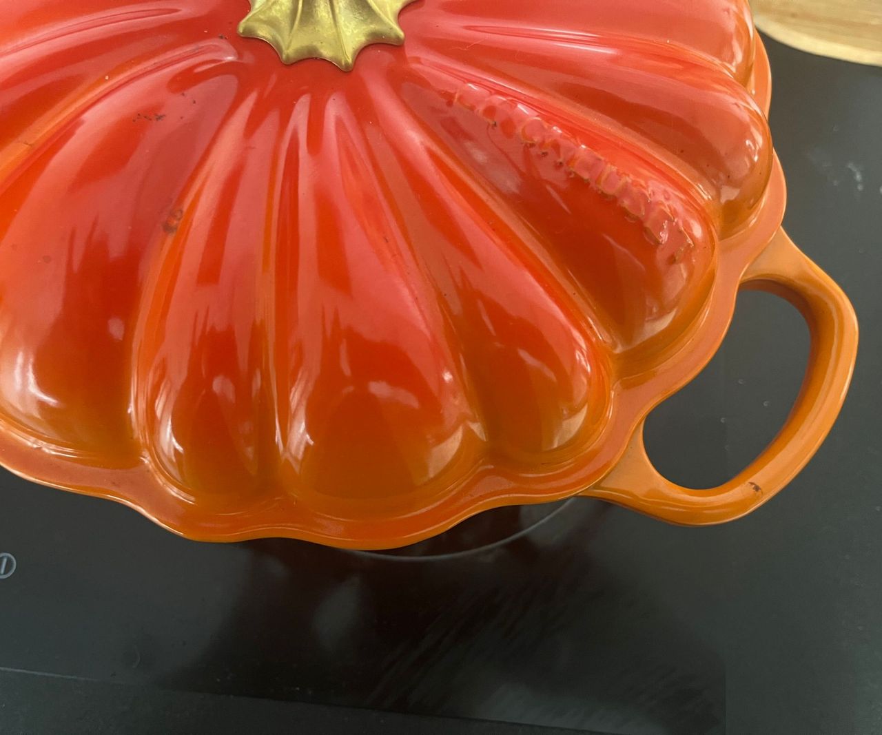 An orange Le Creuset pumpkin Cocotte on a black kitchen stove top
