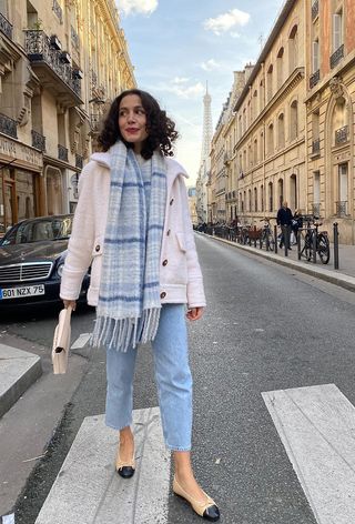 French woman wearing a checked scarf with a white coat and light wash jeans.