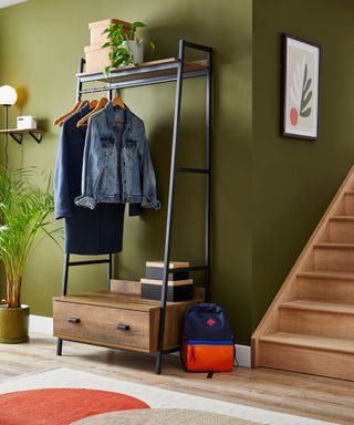 A green entryway with wooden stairs, a coat rack, and wall art