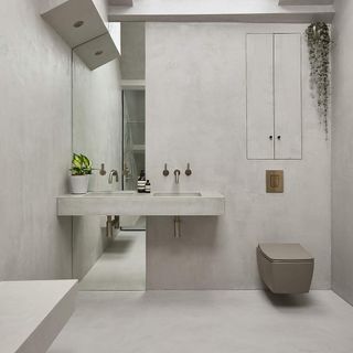 light grey concrete bathroom with full length mirror behind a double vanity sink, with a brown toilet attached to the wall