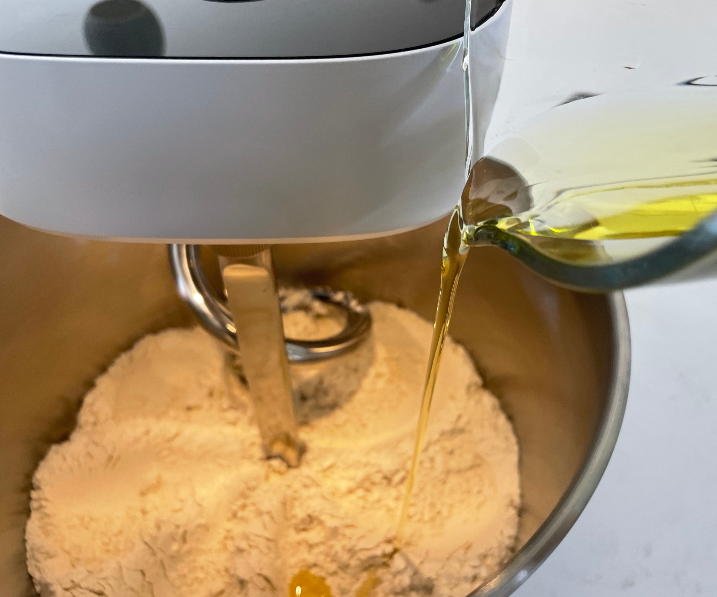 Pouring oil into flour in the Ooni Halo Pro Spiral Mixer to make pizza dough