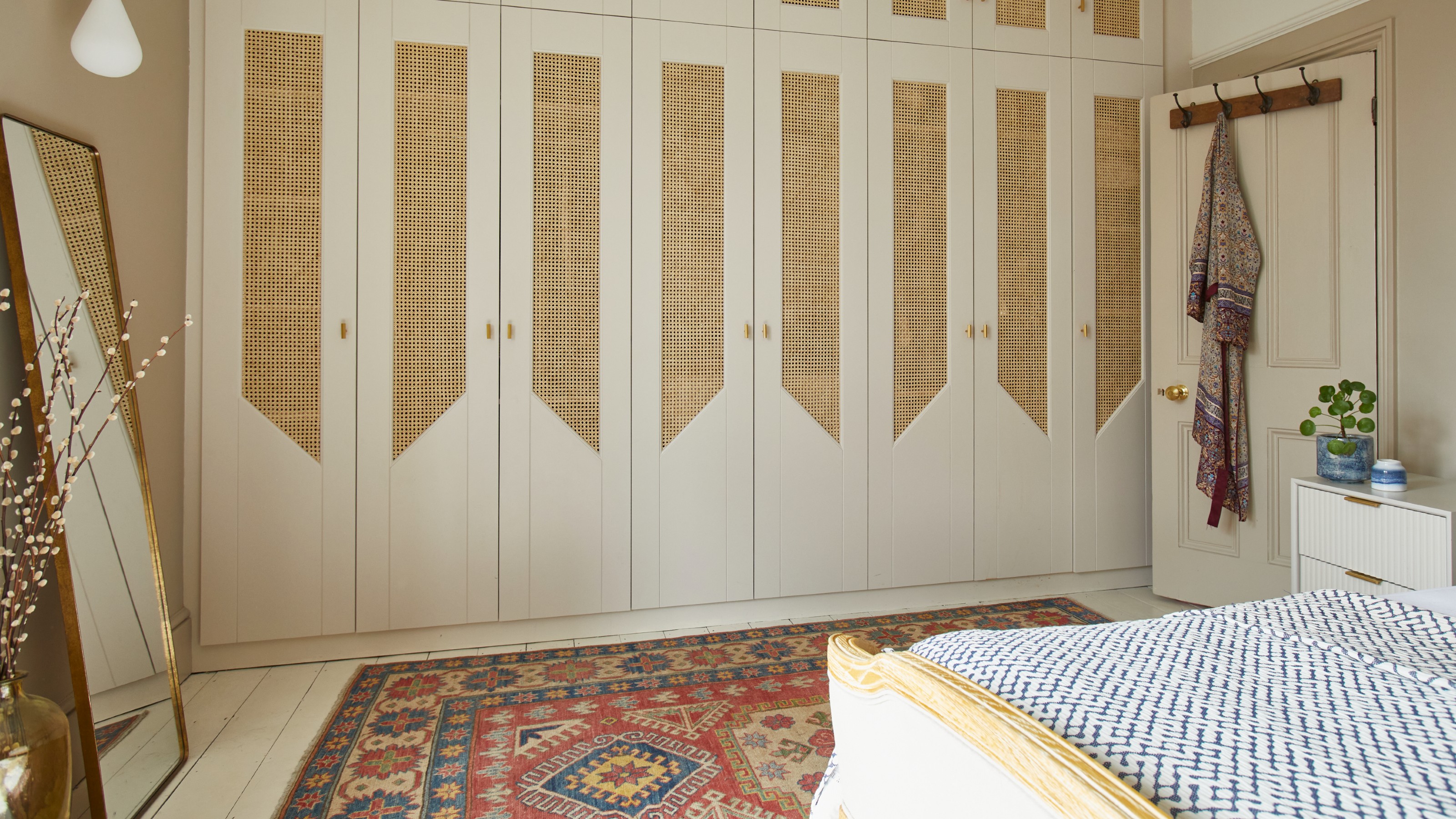 A neutral bedroom with cream-coloured built-in wardrobes covering a whole wall, finished with cane-webbing panels