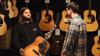 Sales assistant showing a customer an acoustic guitar in a guitar store