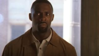 Idris Elba stands in front of a window with a look of concern in The Wire.