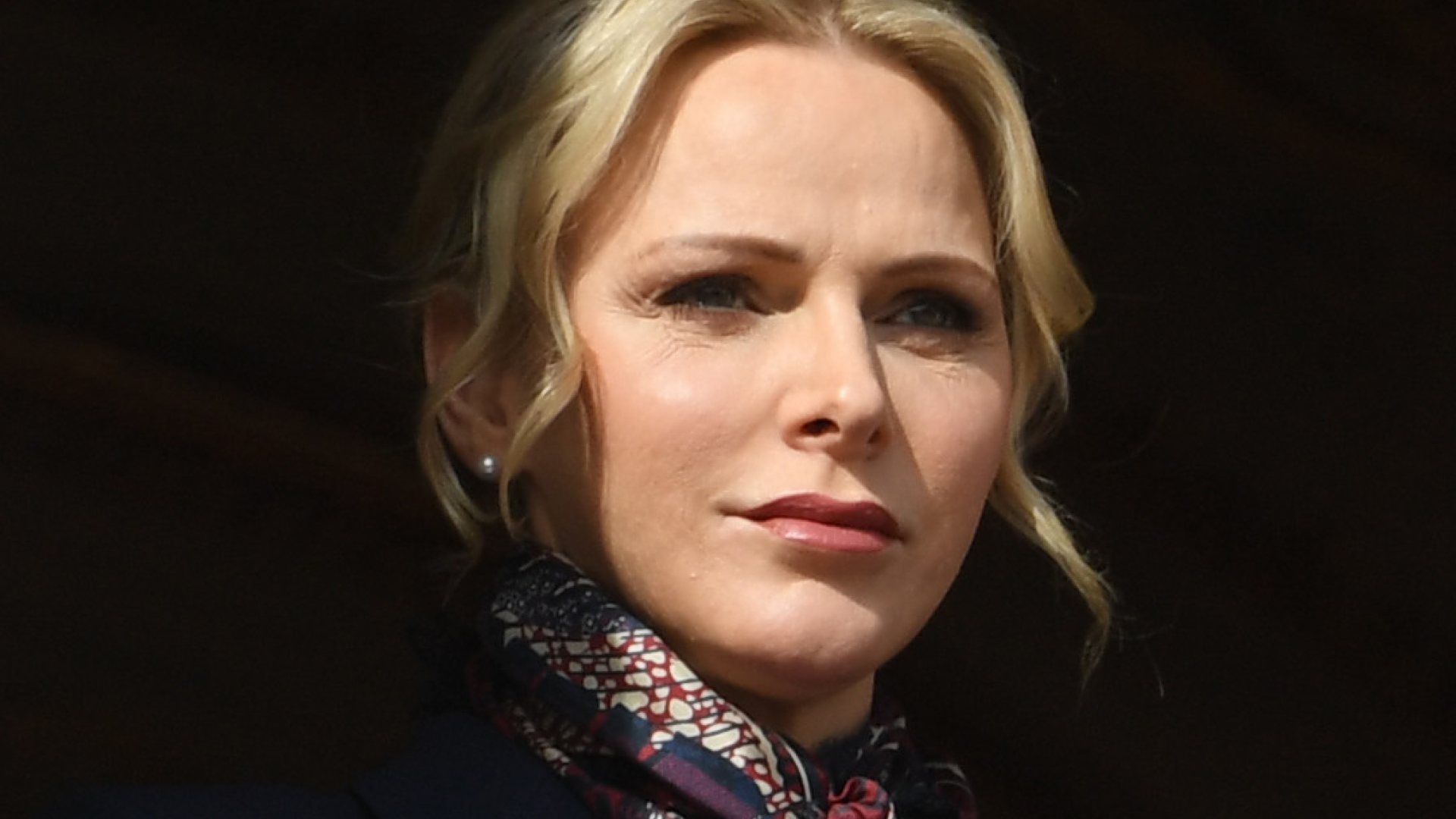Princess Charlene wears a silk scarf and coat and wears her hair tied back