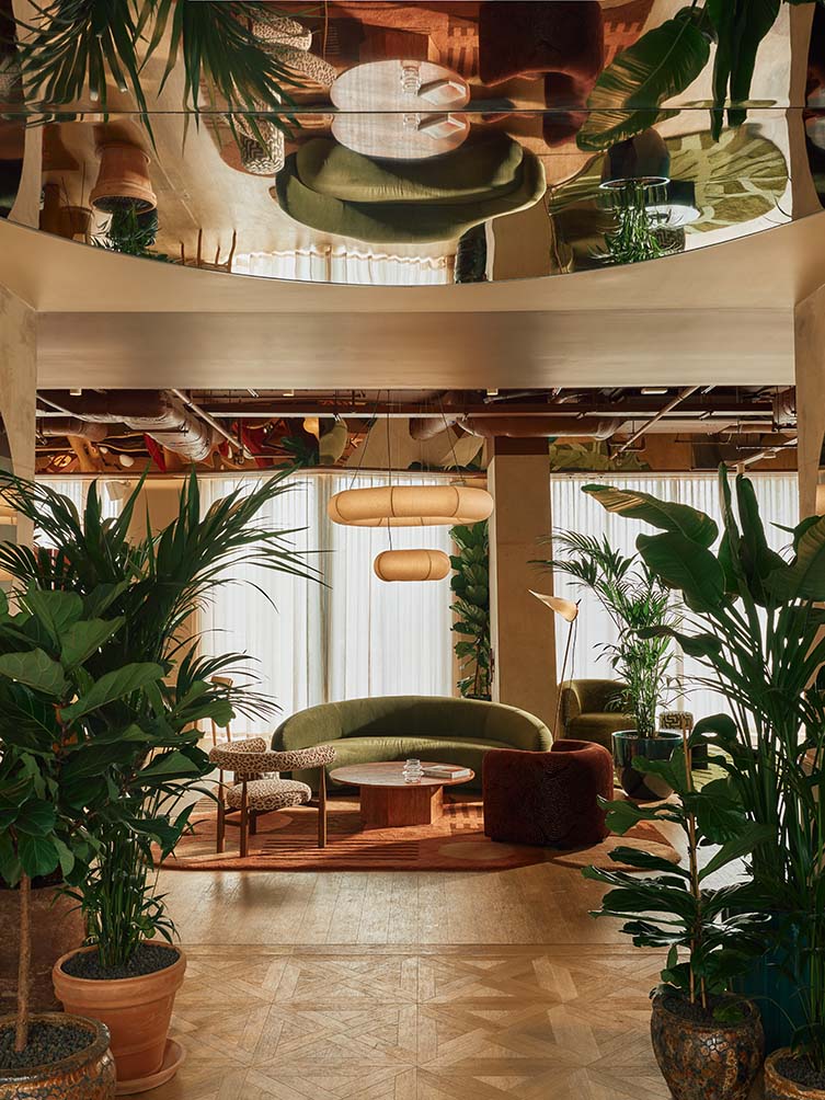 Interior shots of a design hotel decorated with pale woods, plants, industrial-chic furniture, and warm lighting, with spherical sconces and pendant lamps.