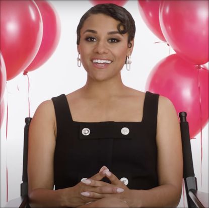 Ariana DeBose in black dress sitting in front of red balloons for Marie Claire's pop quiz video