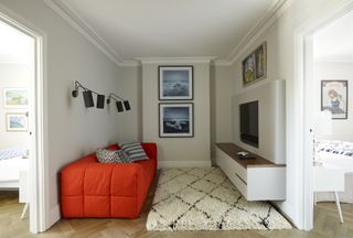 Television snug area with red sofa, wall mounted television and cream rug on parquet flooring