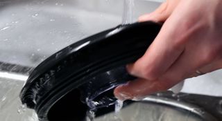 Black lid of a blender being rinsed under a tap