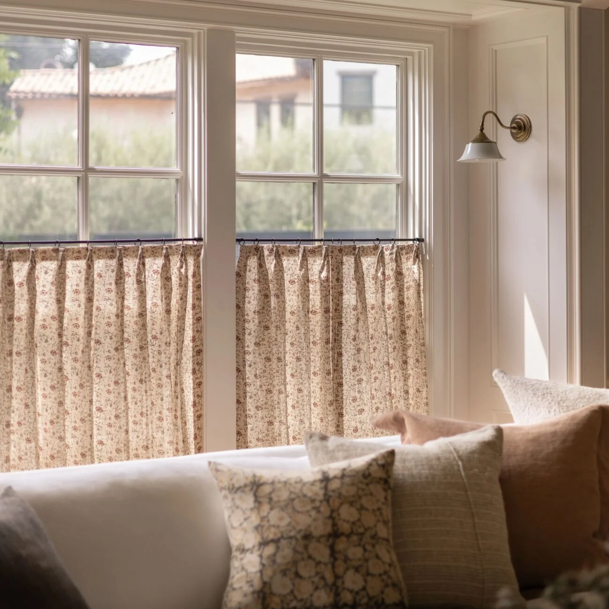 a room with a couch, several pillows, and cafe curtains on the windows