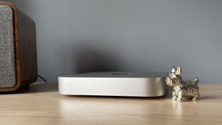 A side view of the Mac mini (M2 Pro) next to a small, gold dog figurine.