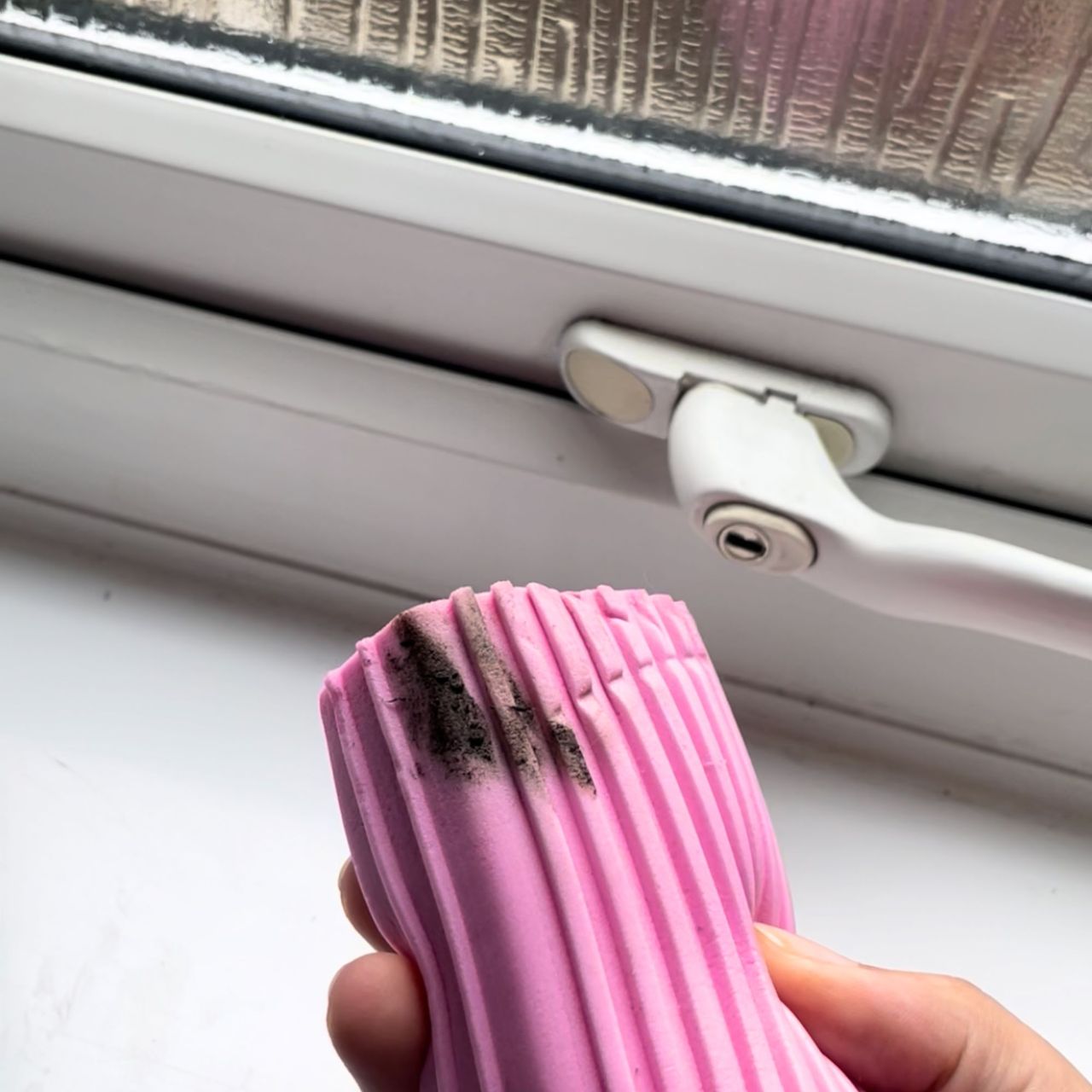 Hand holding dirty Damp Duster in front of bathroom window with black seals