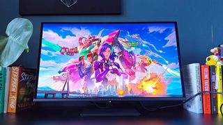 Alienware AW2726DM monitor on black desk with Overwatch loading screen displayed.