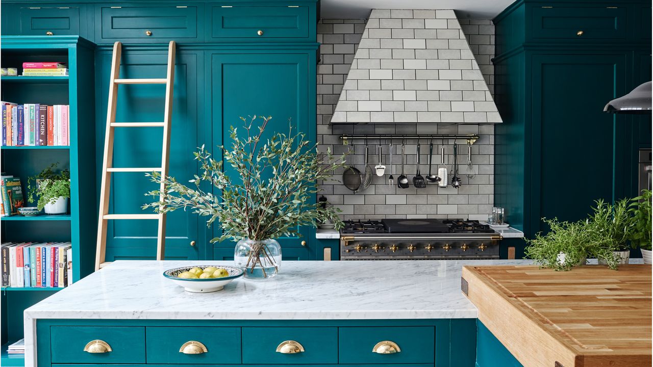 Modern, country kitchen with dark blue walls and units, kitchen island with white and grey marble top, range cooker with extractor tiled in grey