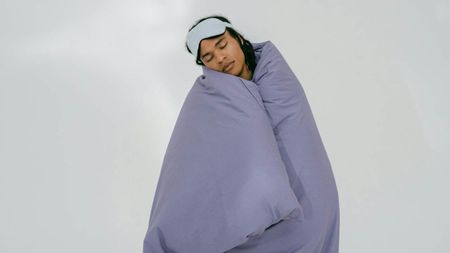 A woman cocooned in a duvet with a sleep mask on