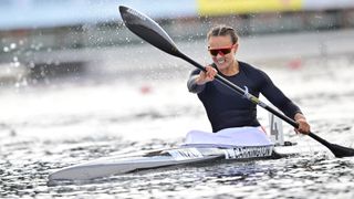 Lisa Carrington, in a black top and mirrored sunglasses, races her canoe ahead of the 2024 Paris Olympic Games Canoe Sprint. 