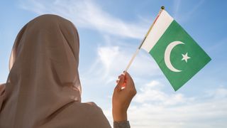 Silhouette of muslim woman in head scarf with Pakistan flag at blue sunset sky