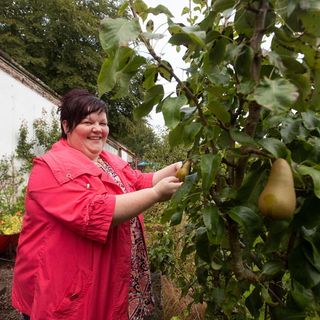 a lady in a red jacket tending to a plant in her garden