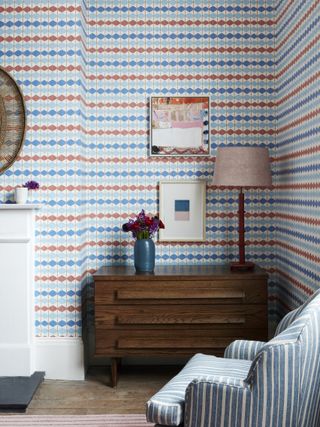 living room with geo stripe wallpaper in blues and red, stripe blue armchair, retro chest of drawers, artwork, lamp