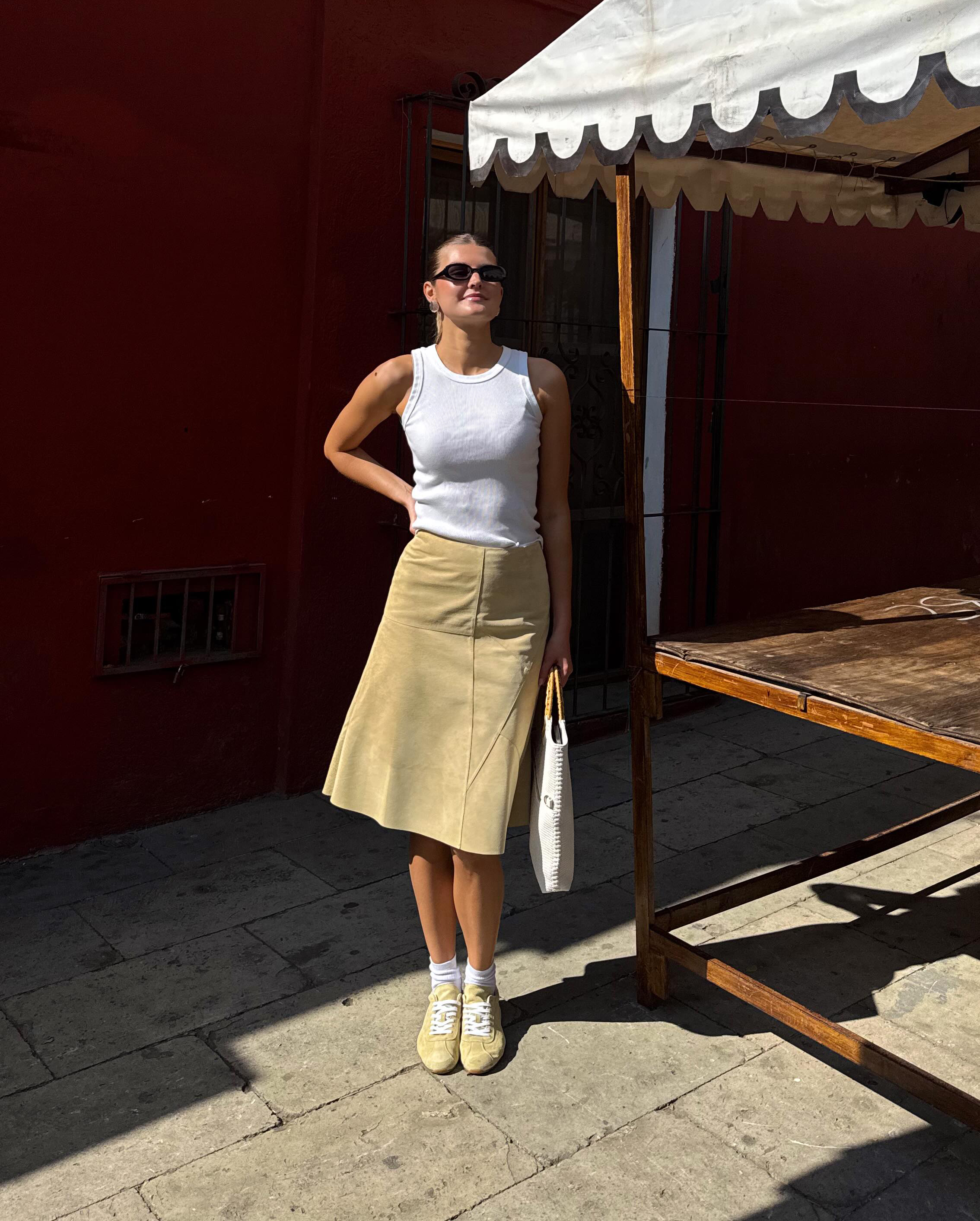 @styledbysara wears a pair of pale yellow trainers with a yellow midi skirt and white vest top