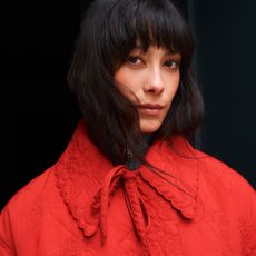 Model wearing a red collared, quilted jacket from Damson Madder sold at Fenwick