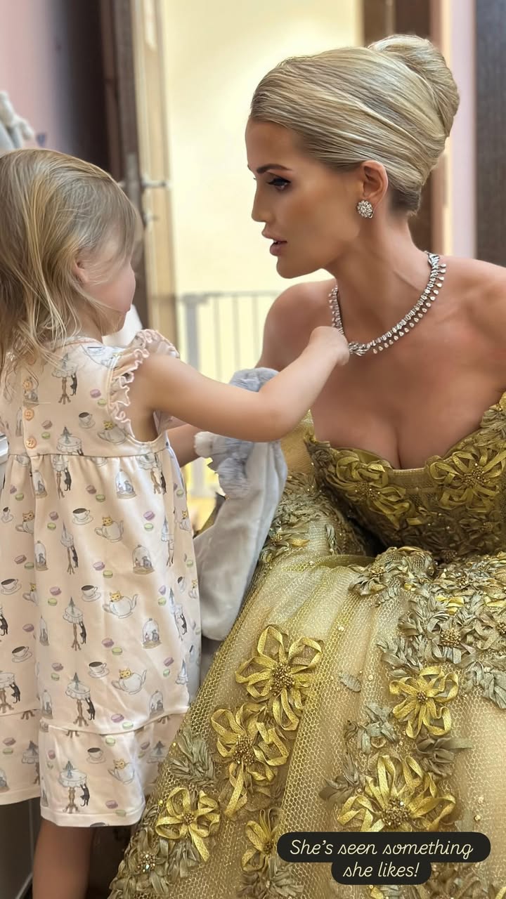 Kitty Spencer bending in front of her daughter wearing a gold gown and diamond necklace