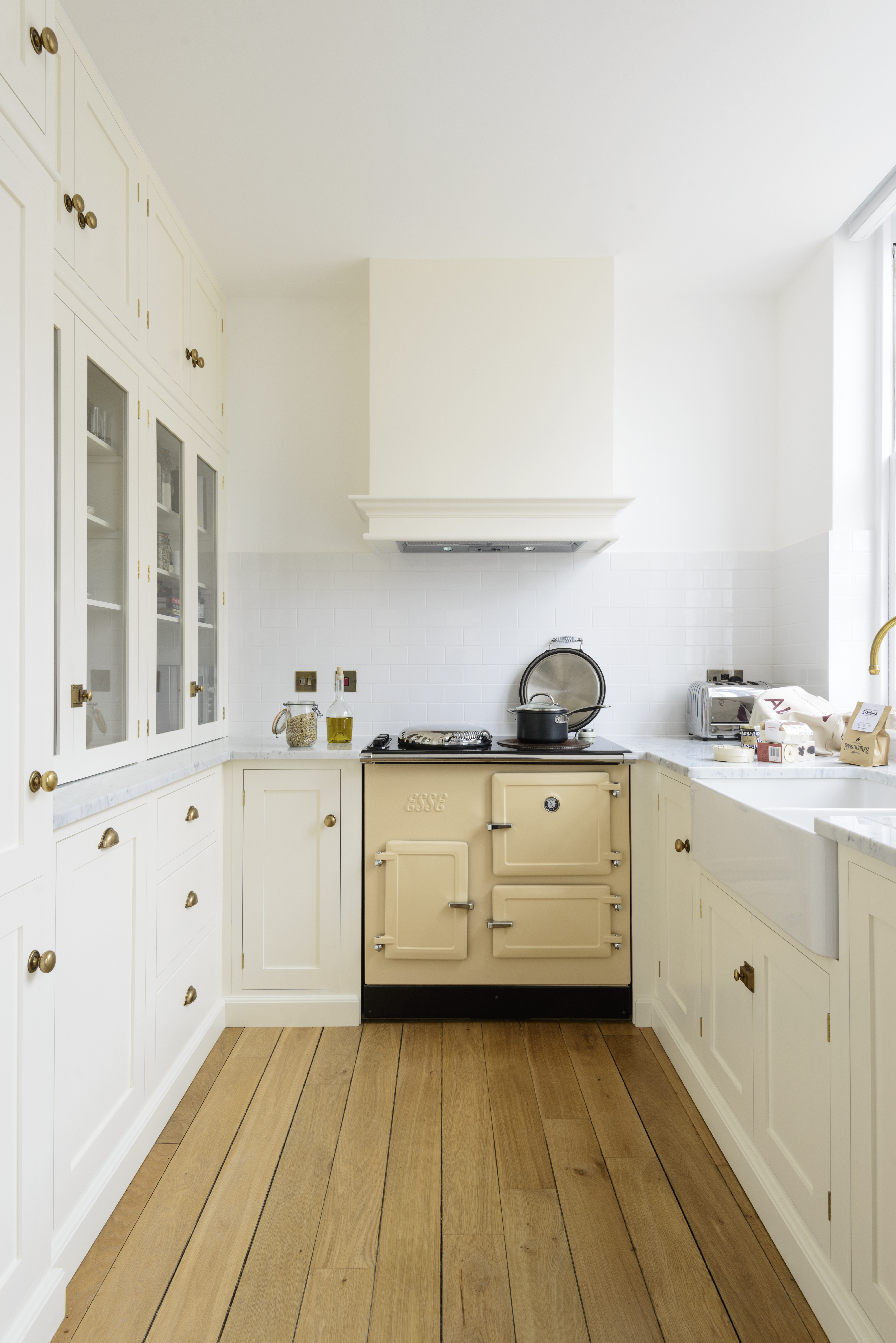 An all-white galley kitchen with brass hardware and wooden flooring