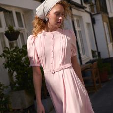 Model wearing a baby pink puff sleeve dress with matching belt sold at Ghost with a bandana in front of houses