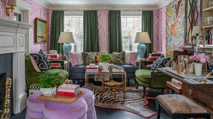 A living room with pink and white wallpaper, green curtains, artwork and an eclectic mix of multicolored wallpaper in a maximalist style