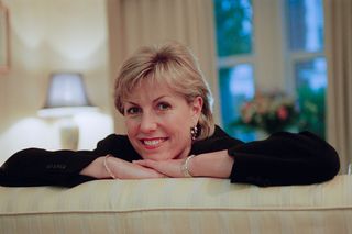 Jill Dando leaning on a sofa with arms folded, smiling at the camera