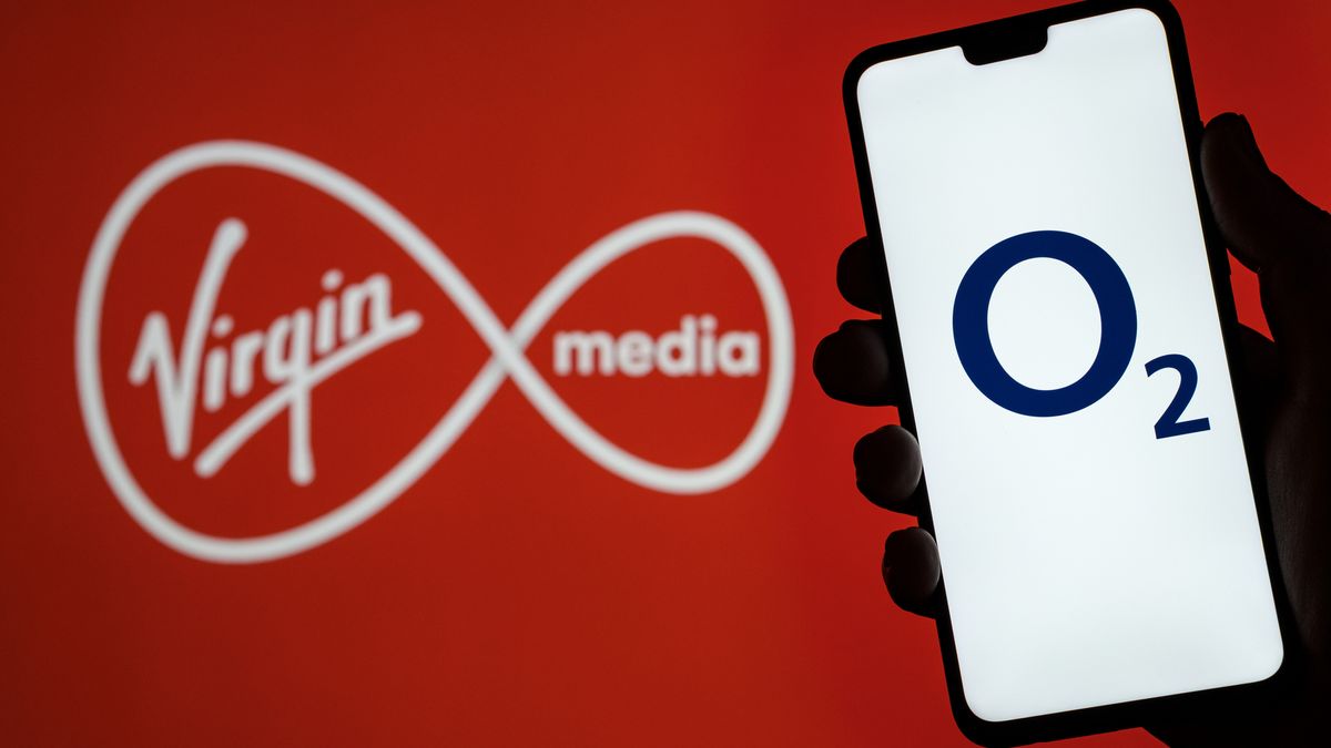 O2 Telefonica logo on smartphone screen hold in hand and Virgin Media logo on blurred background