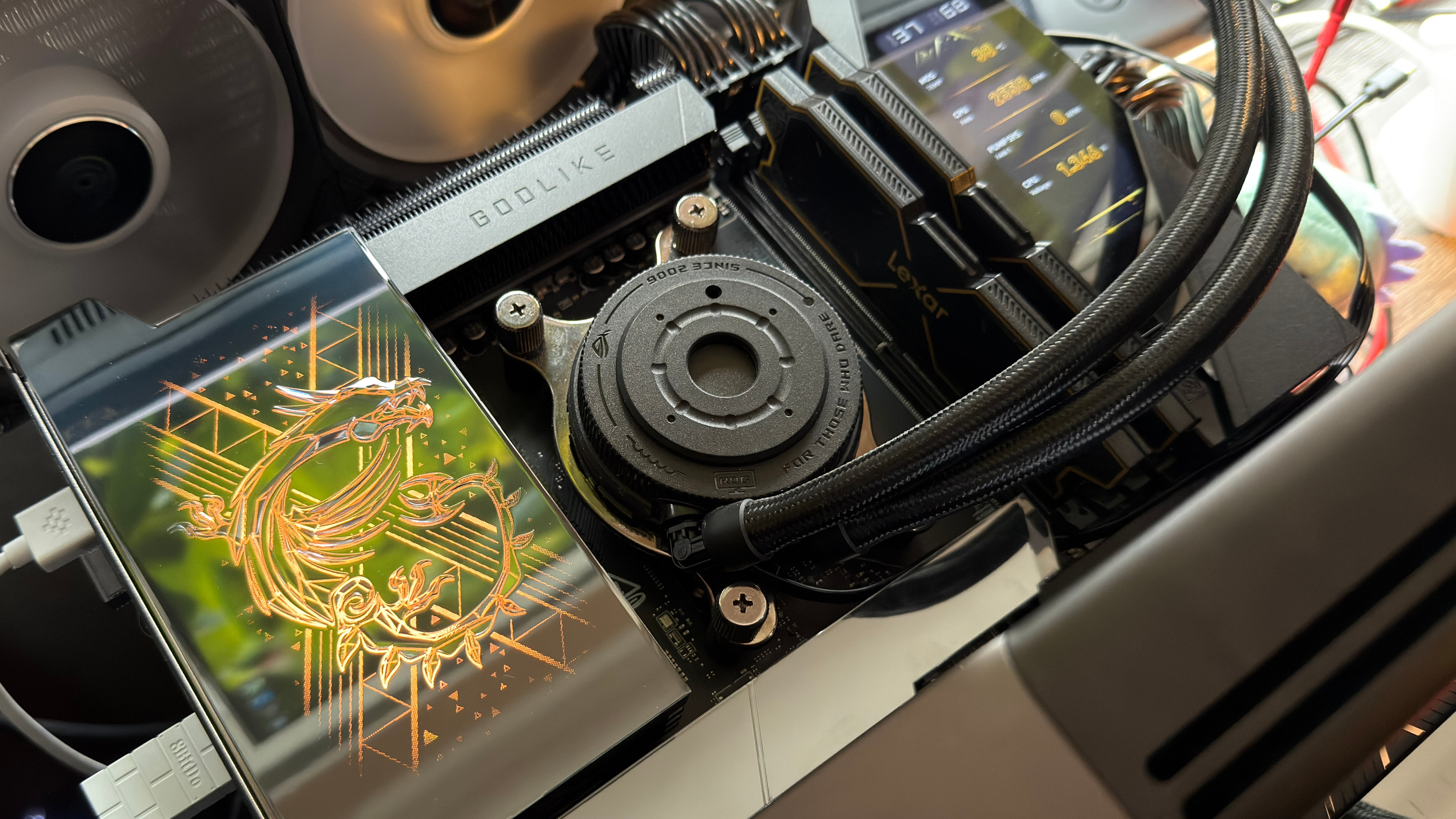 A close-up photograph of an open test bench PC, show a high-end motherboard, a simple AIO cooler, and a 32 GB kit of DDR5 memory.