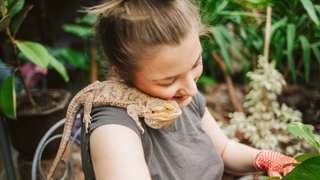 Bearded dragon sitting on a girl's shoulder around greenery, one of the best pet reptiles