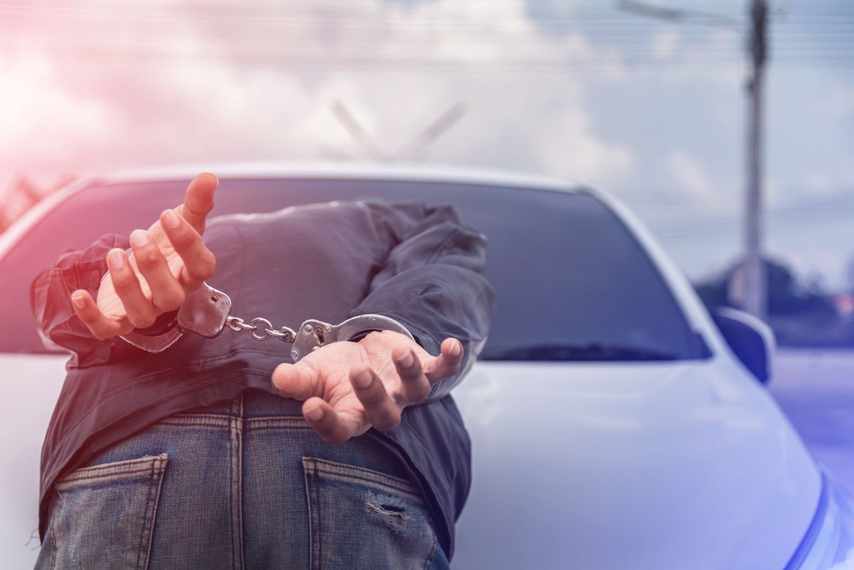 Handcuffed person face-down on the hood of a police car