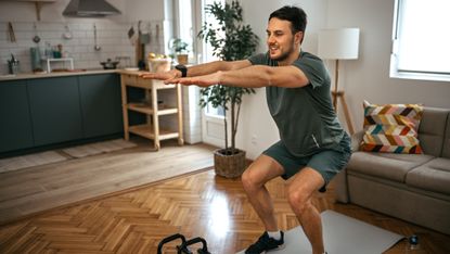 Man doing bodyweight squats at home in living room