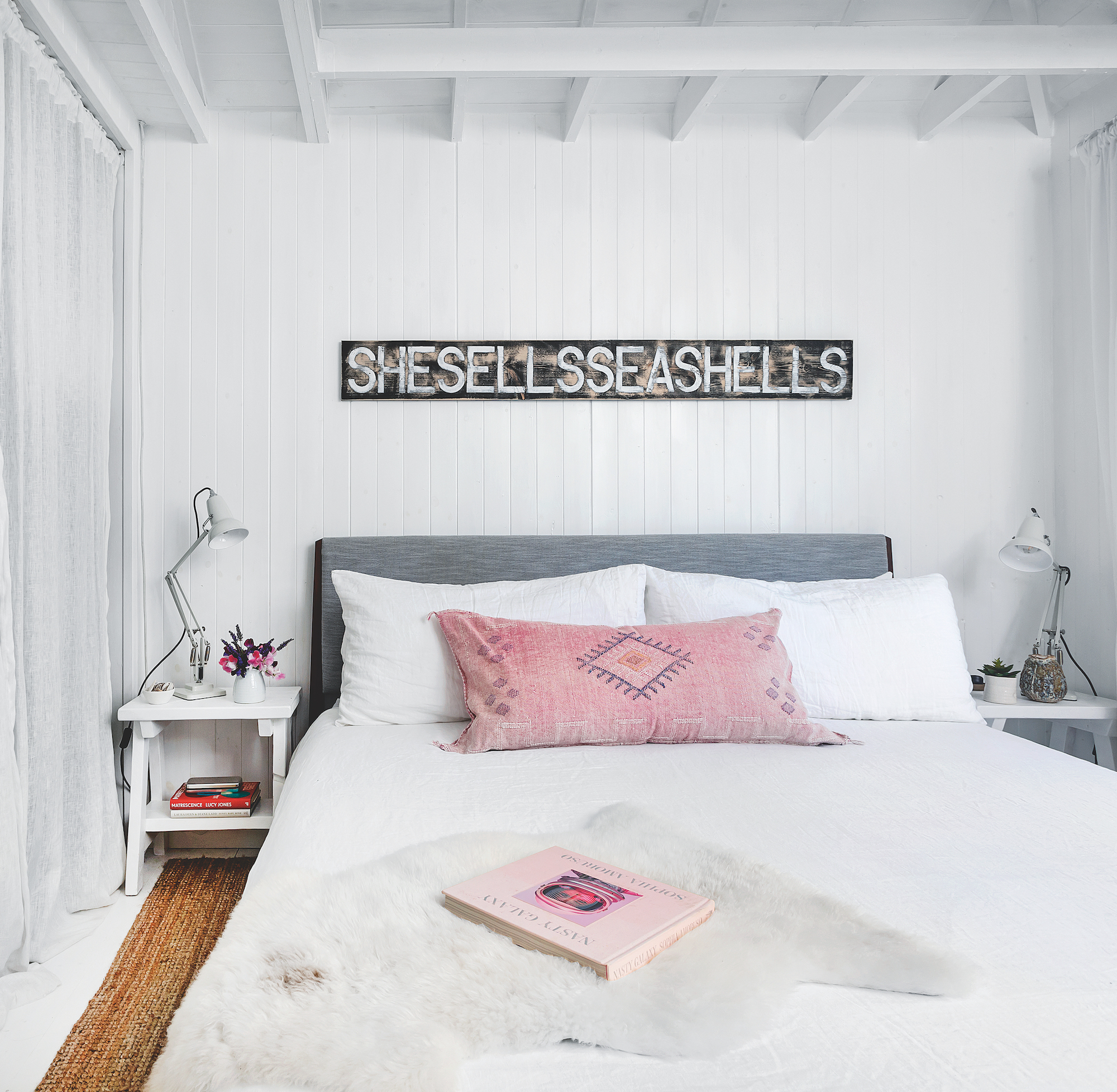 Coastal style bedroom with white wood panel walls, white side tables with anglepoise lamps and vintage sign on wall