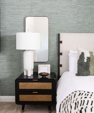 Modern bedroom with gray walls, neutral bedding, large table lamp and mirror behind