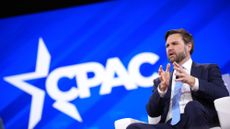 JD Vance, seated, at the CPAC convention. He is wearing a dark-blue suit with a white buttondown shirt and a light-blue tie. He is gesturing with his hands