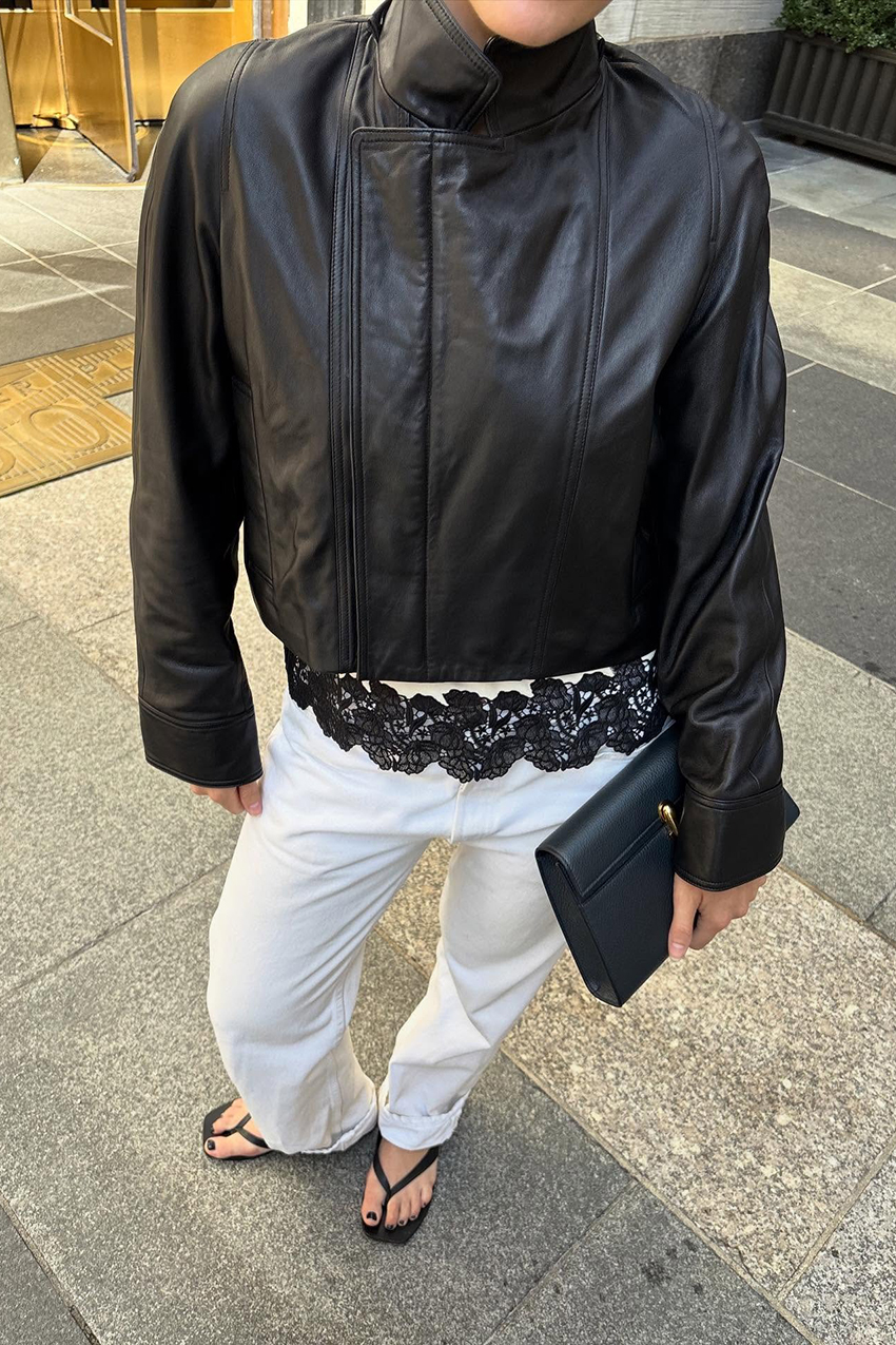 A woman wearing a leather jacket, white pants, and a lace tank top
