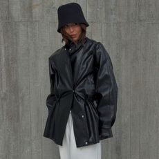 A woman wearing a black leather jacket, white trousers and a stylish black hat