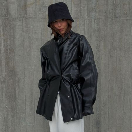 A woman wearing a black leather jacket, white trousers and a stylish black hat