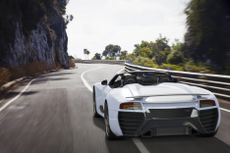 A white sports car navigating the winding curves of the Great Ocean Road in Victoria, Australia.