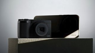 A ricoh GR compact camera alongside a Realme smartphone, on a green concrete plynth