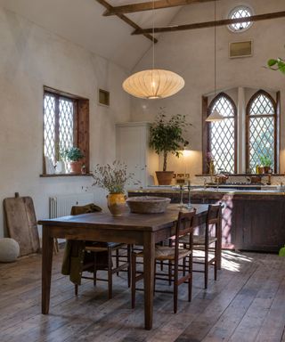 Traditional kitchen with dark wooden flooring, wooden features, and large dining table, two pendant lights, wooden beams, traditional arch windows