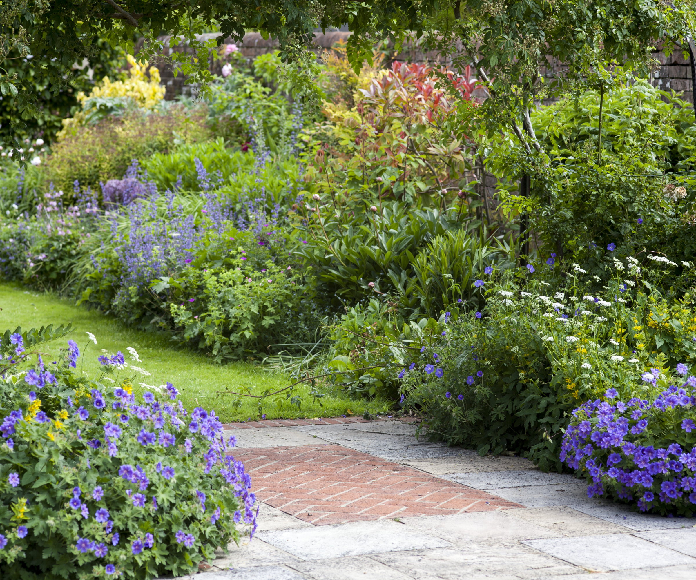 A brick patio connected to a lawn surrounded by flower beds