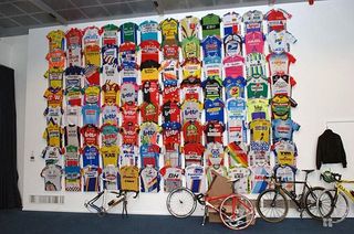 A few Museeuw bikes await assembly in front of a vast wall of jerseys in the Centrum Ronde Van Vlaanderen.