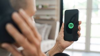 A woman holding a smartphone with Spotify app