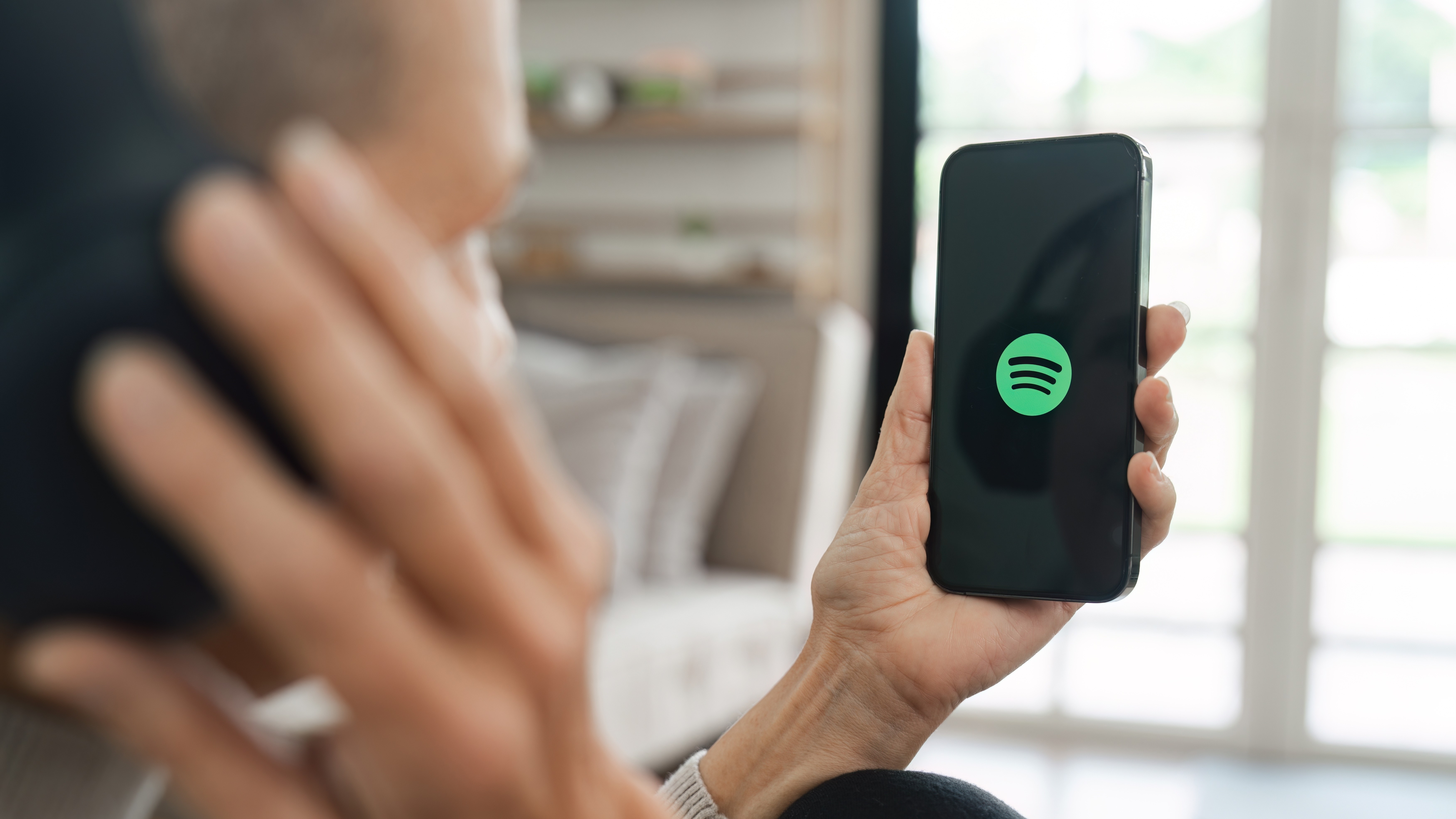 A woman holding a smartphone with Spotify app