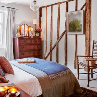 a traditional cottage bedroom with original details bed covered in layers of cosy bedding and a chest of drawers with mirror and candles